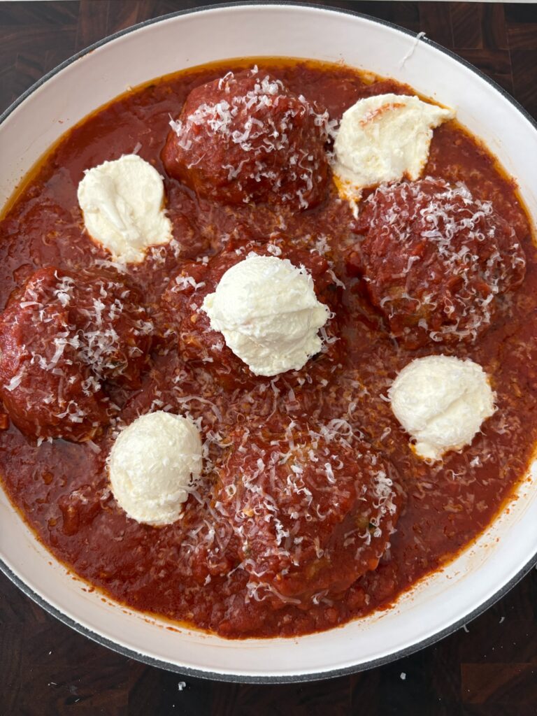 Family-style ricotta meatballs baked in sauce with extra ricotta on top.