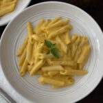 butternut squash pasta in a white bowl garnushed with fresh bail on a cutting board with a with folded napkin