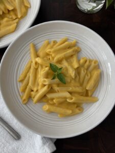 butternut squash pasta in a white bowl garnushed with fresh bail on a cutting board with a with folded napkin