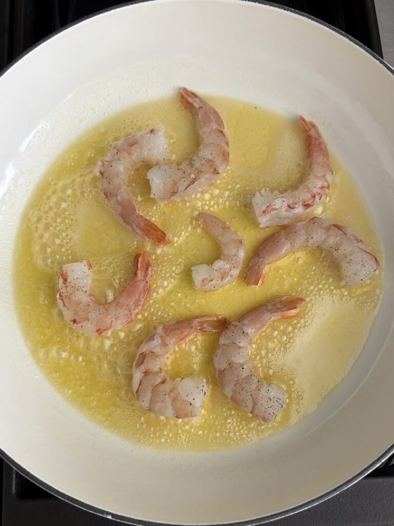 Shrimp cooking in olive oil and garlic in a white pan
