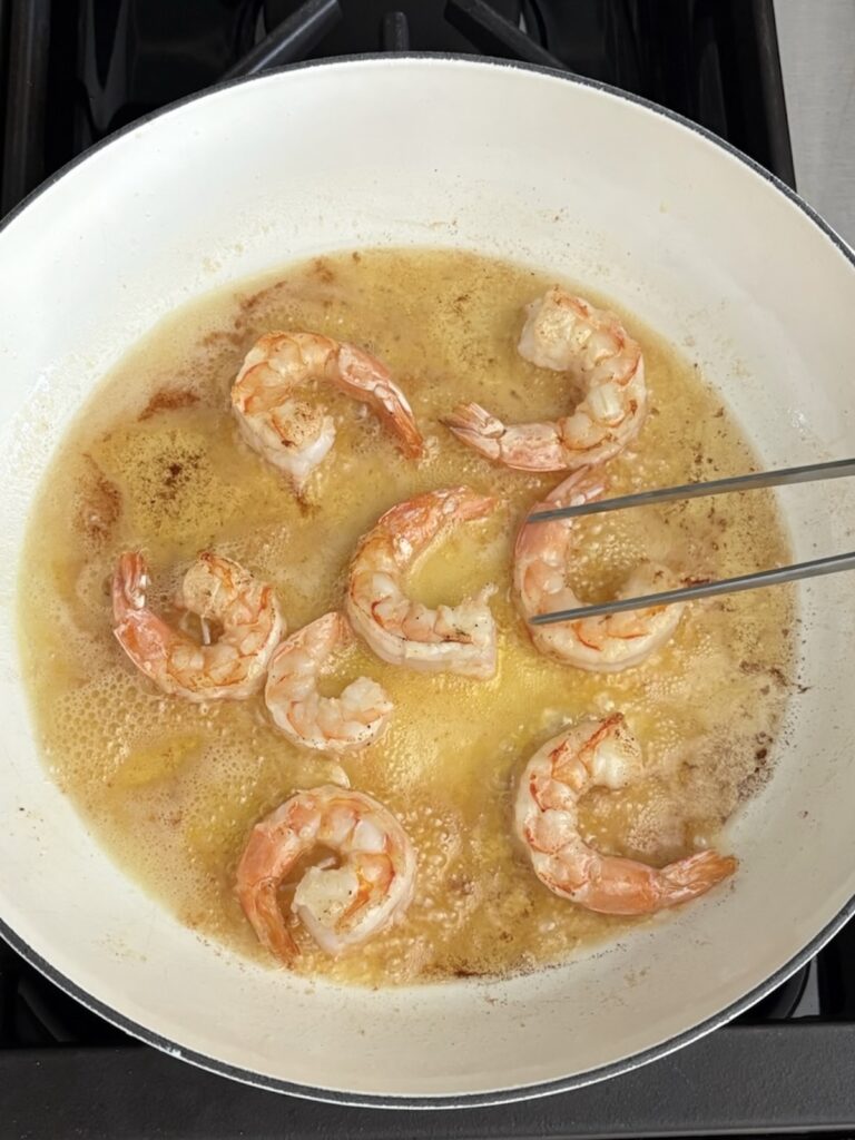 Shrimp sautéing in garlic butter in a white skillet for creamy pasta