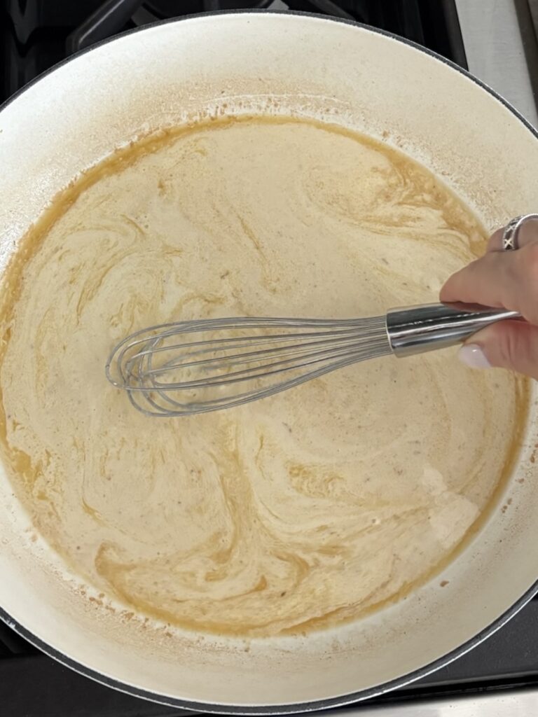 Whisking creamy garlic sauce in a skillet to prepare shrimp pasta