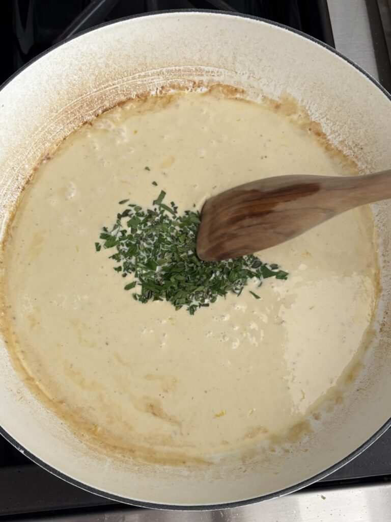 Stirring fresh chopped herbs into a creamy garlic sauce for shrimp pasta