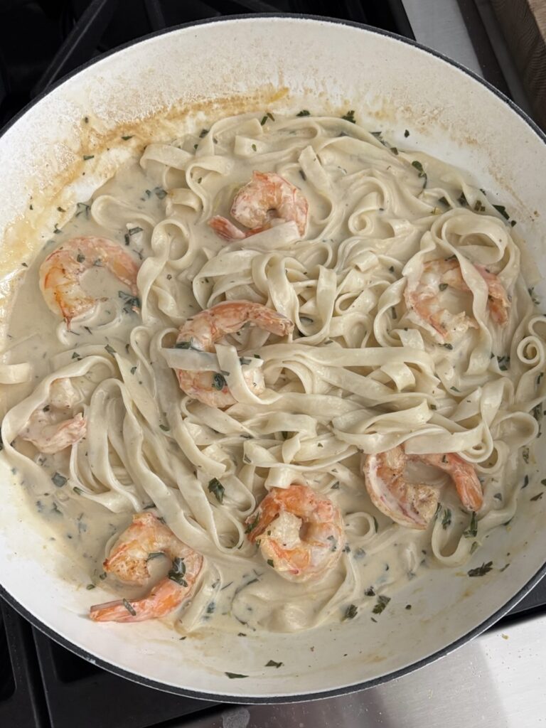 Creamy garlic shrimp pasta with herbs and lemon in a white skillet
