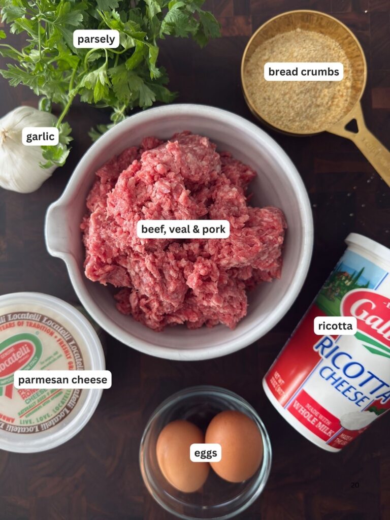 Ingredients for baked ricotta meatballs including ground beef, veal, and pork mix, fresh garlic, ricotta cheese, Parmesan cheese, breadcrumbs, and eggs, are displayed on a dark cutting board.