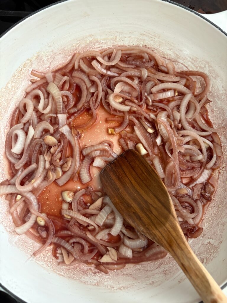 Sliced red onions sautéing in olive oil with a wooden spoon in a white skillet for Steak Pizzaiola
