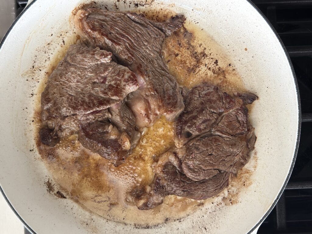 Thin-cut steak searing in a white pan for Steak Pizzaiola, showing golden brown crust and rendered fat