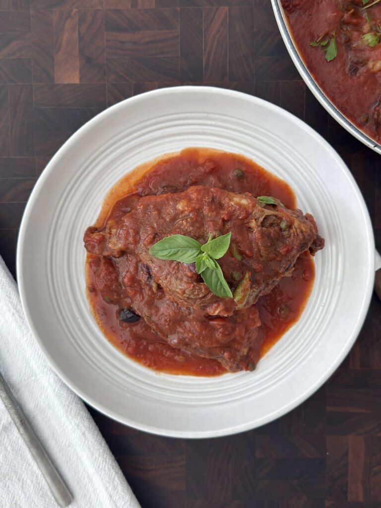 Steak Pizzaiola served in a white bowl with tomato sauce and fresh basil on top