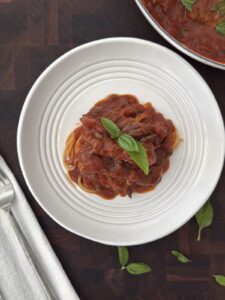 Steak Pizzaiola served over spaghetti in a white bowl with tomato sauce and fresh basil on top