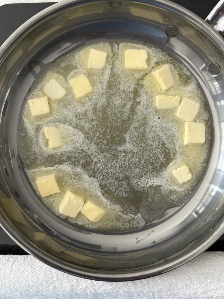 Cubes of butter are melting in a stainless steel skillet to make a brown butter sage sauce for ravioli.