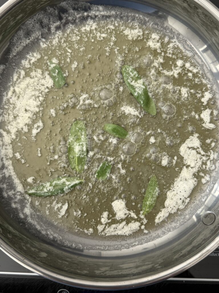 Brown butter bubbling in a skillet with fresh sage leaves for butternut squash ravioli sauce.