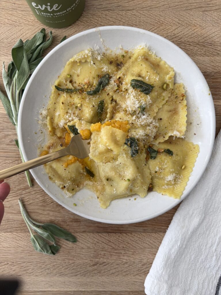 Fork cutting into homemade butternut squash ravioli with golden brown butter sage sauce