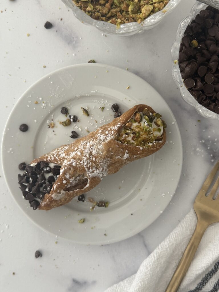 Classic Italian cannoli filled with sweet ricotta cream, dipped in mini chocolate chips, and dusted with powdered sugar.