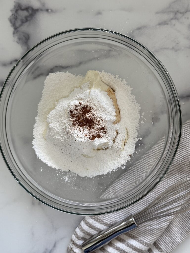 A glass bowl with ricotta cheese, powdered sugar, vanilla, and cinnamon is being mixed together for homemade Italian cannoli filling.