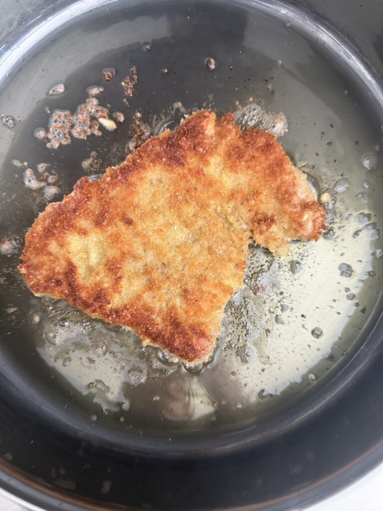 Golden brown pork cutlet frying in a pan with hot oil for pork Milanese.