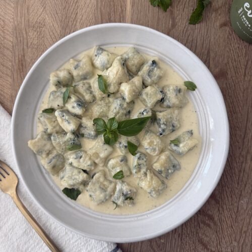 Homemade spinach and ricotta gnocchi served in a creamy sauce, garnished with fresh basil for an authentic Italian meal.