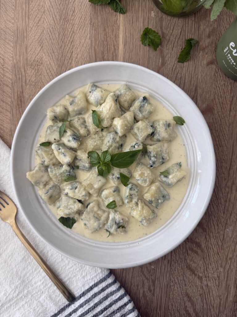 Homemade spinach and ricotta gnocchi served in a creamy sauce, garnished with fresh basil for an authentic Italian meal.
