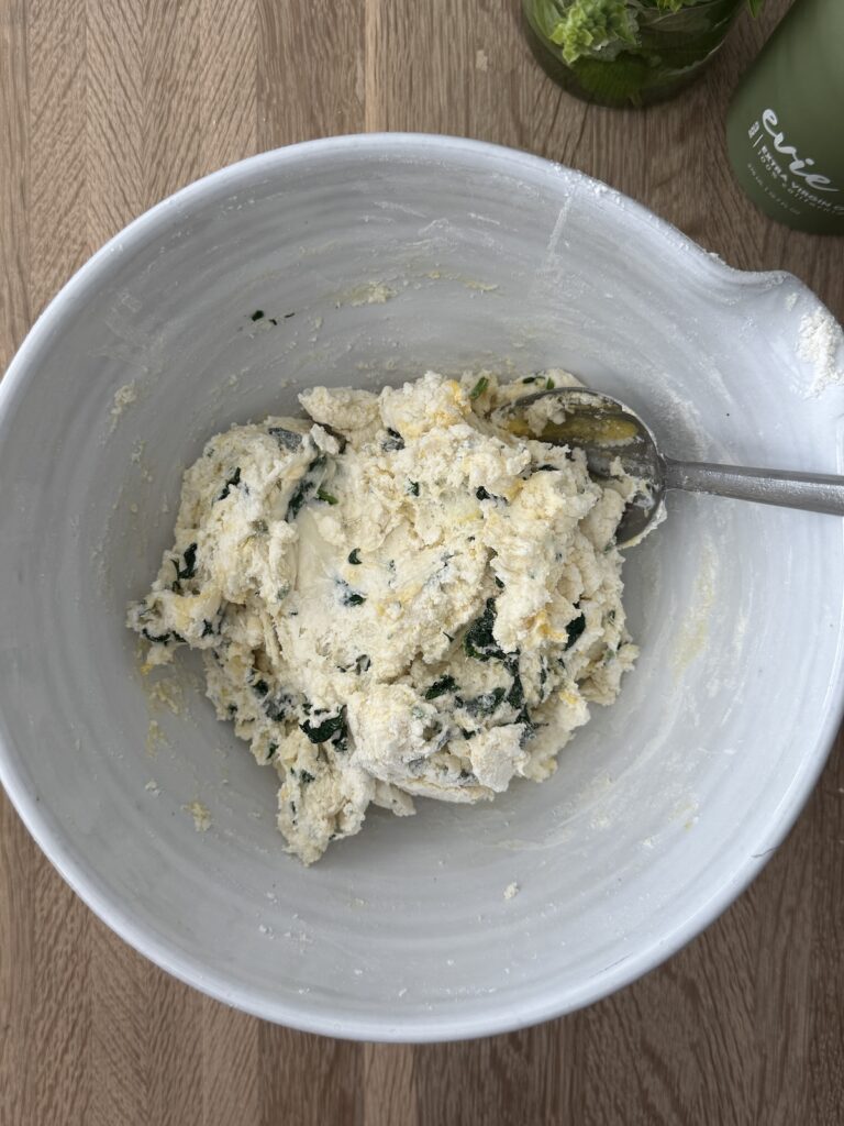 Spinach and ricotta gnocchi dough mixture in a white bowl, combining ricotta cheese, spinach, flour, and Pecorino.