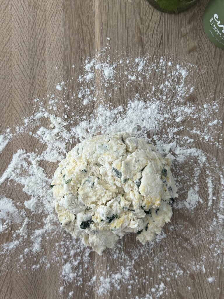 Spinach and ricotta gnocchi dough resting on a floured wooden surface, ready to be kneaded.