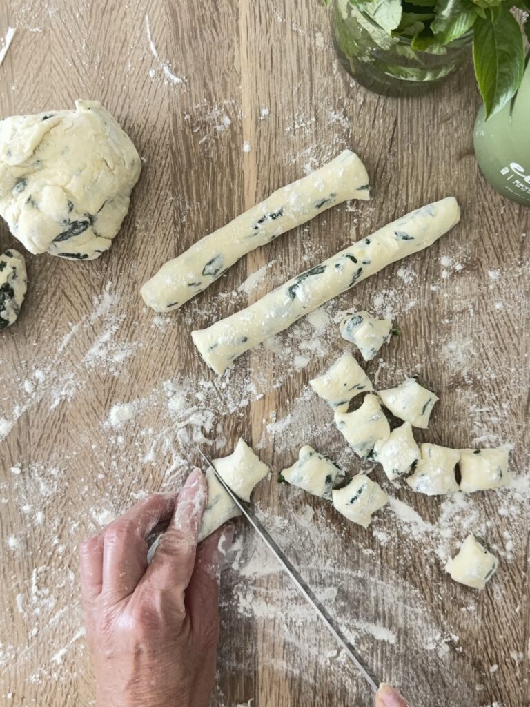 Hand cutting homemade spinach and ricotta gnocchi dough into small pieces on a floured wooden surface, showing the process of making traditional Italian gnocchi.