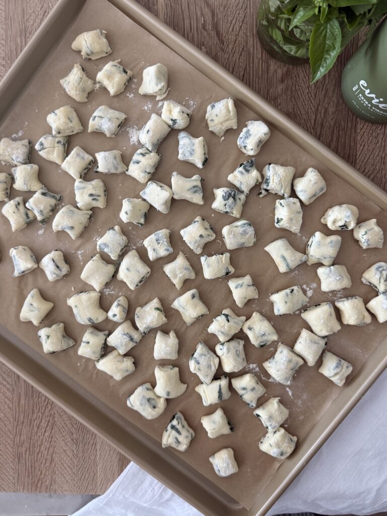Homemade spinach and ricotta gnocchi pieces arranged on a baking sheet, ready to cook. Light, fluffy Italian dumplings made with fresh spinach, ricotta cheese, and flour