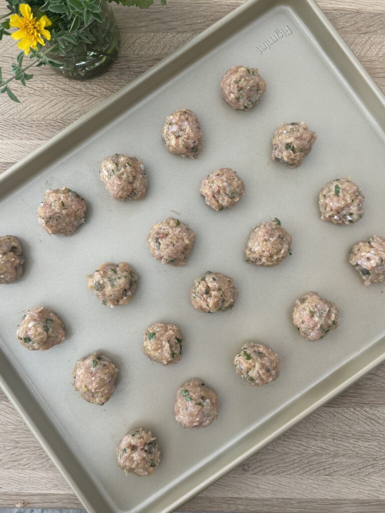 Rolled chicken piccata meatballs on a sheet pan, ready to cook.