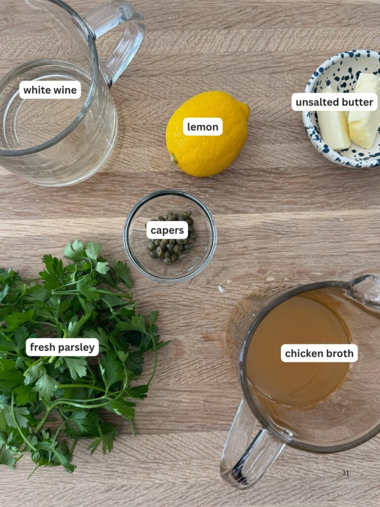 Chicken piccata meatballs sauce ingredients—white wine, lemon, unsalted butter, chicken broth, capers, and fresh parsley—flat lay on wood.