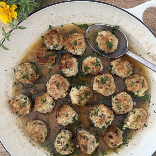 Chicken piccata meatballs in lemon-caper butter sauce in a skillet, garnished with parsley, with a spoon lifting one meatball.