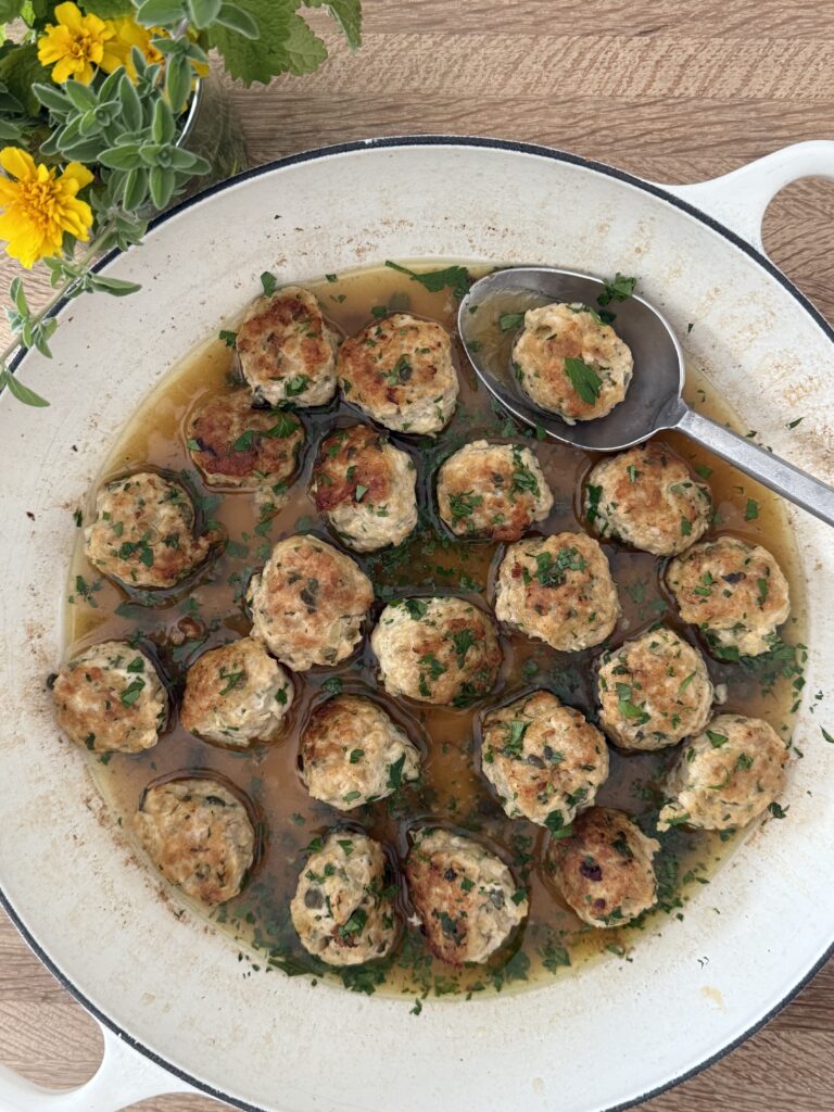 Chicken piccata meatballs in lemon-caper butter sauce in a skillet, garnished with parsley, with a spoon lifting one meatball.