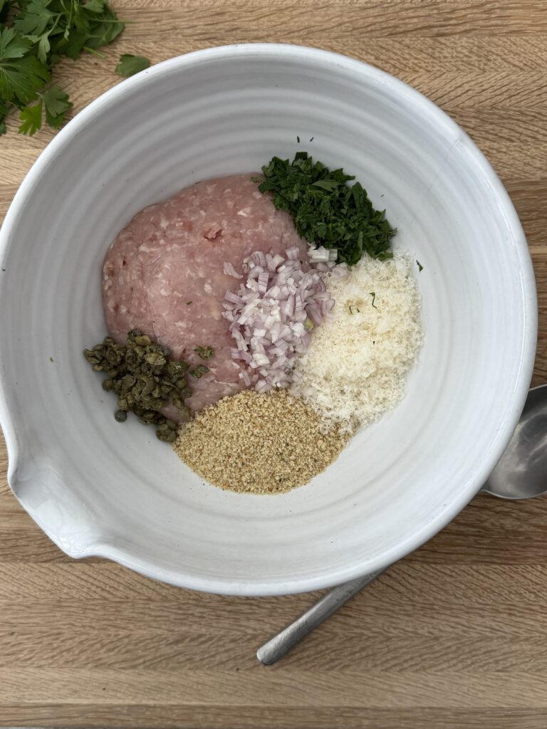 Chicken piccata meatballs mixture—ground chicken, breadcrumbs, Parmesan cheese, shallot, parsley, and capers—in a mixing bowl.