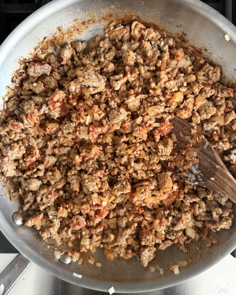 A large skillet showing the browned meats after adding the tomato paste, onion, and garlic-ready to be added to the slow cooker.