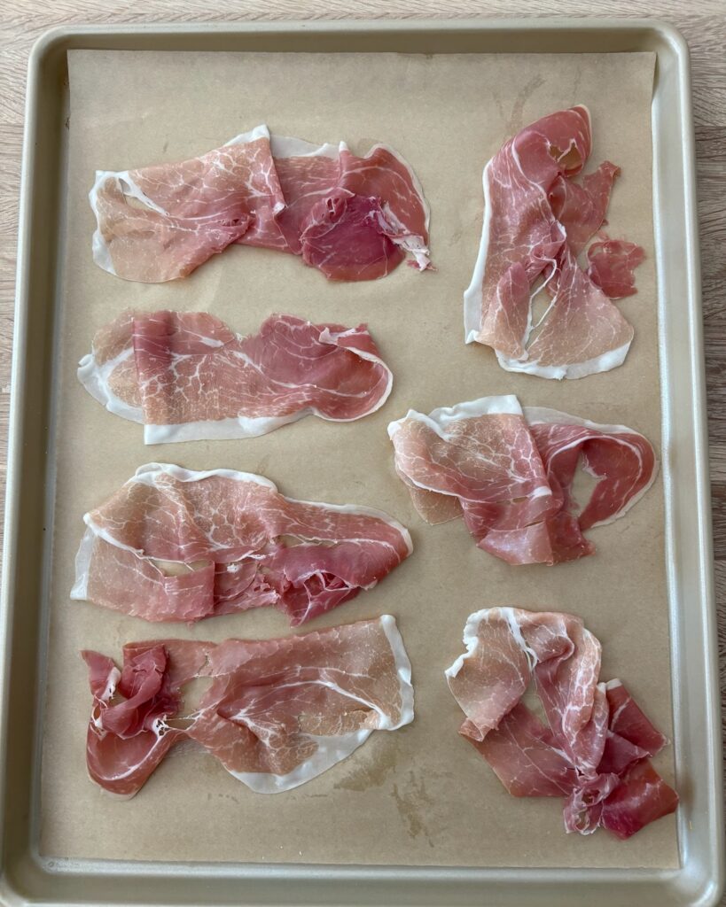 Thin slices of prosciutto on a parchment-lined baking sheet, ready to be baked until crispy for pumpkin risotto.
