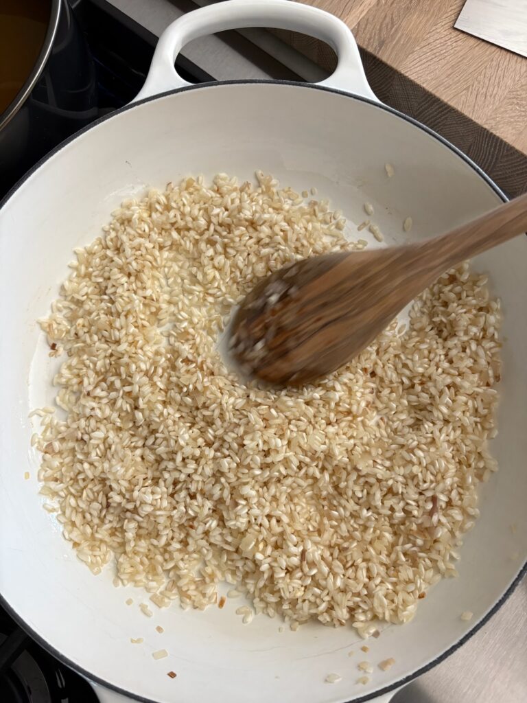 Arborio rice toasting in a white pan on the stove with olive oil for pumpkin risotto.