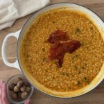 Creamy pumpkin risotto topped with crispy prosciutto and fresh nutmeg on a wooden board.