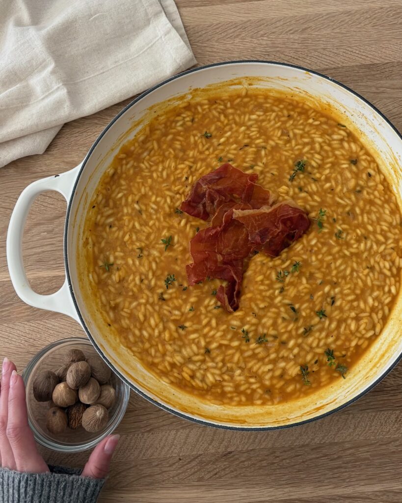 Creamy pumpkin risotto topped with crispy prosciutto and fresh nutmeg on a wooden board.