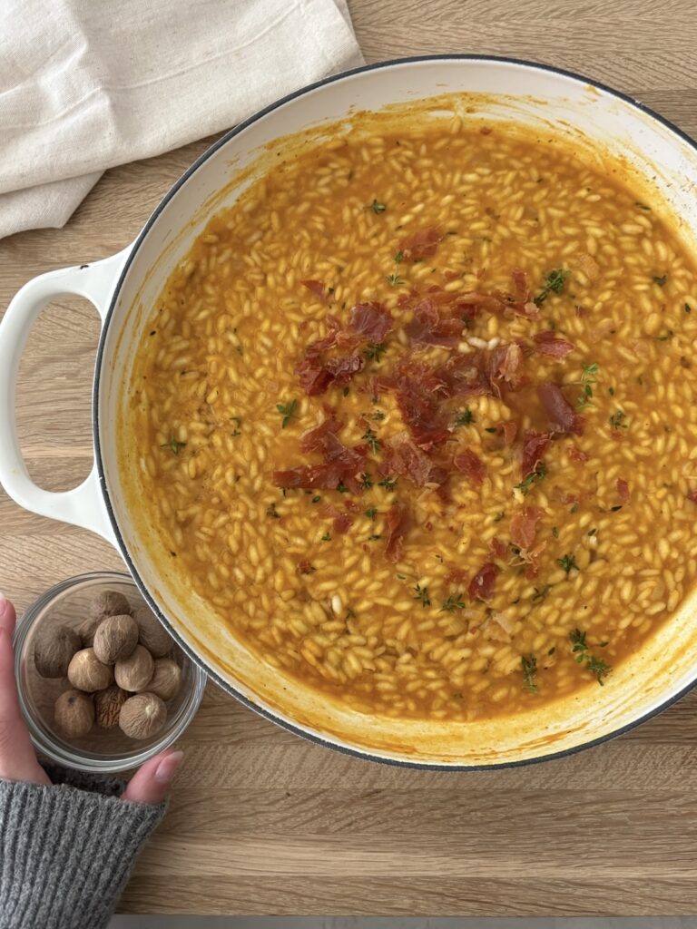 Creamy pumpkin risotto topped with crispy prosciutto and fresh thyme, ready to serve.