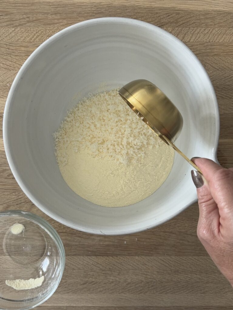 Pouring semolina flour into a mixing bowl with a gold measuring cup on a wooden surface.