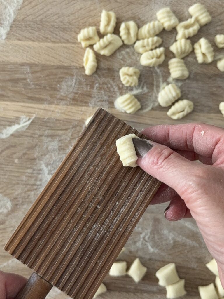 Hand shaping semolina pasta on a wooden gnocchi board.