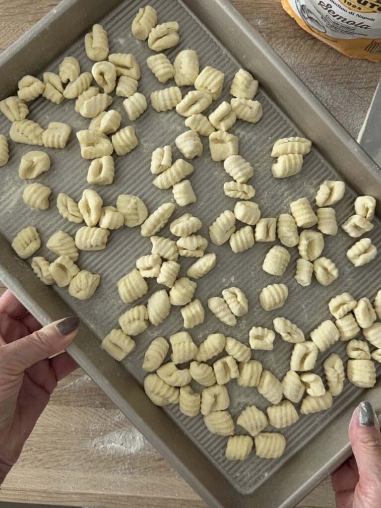 Tray of freshly shaped semolina pasta pieces resting on a floured surface before cooking.