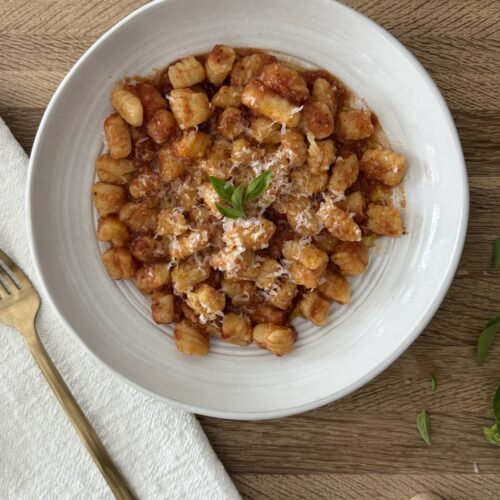 Bowl of homemade semolina pasta topped with tomato sauce, Parmesan cheese, and fresh basil.