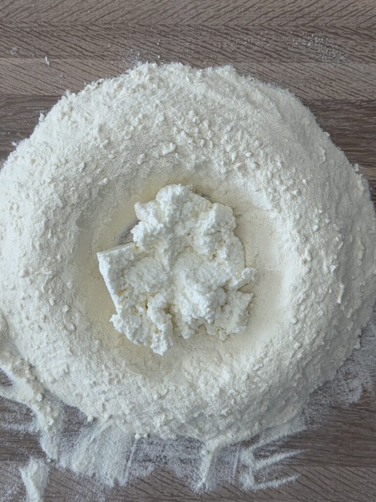 Well of semolina flour with ricotta in the center on a wooden surface with a fork nearby.