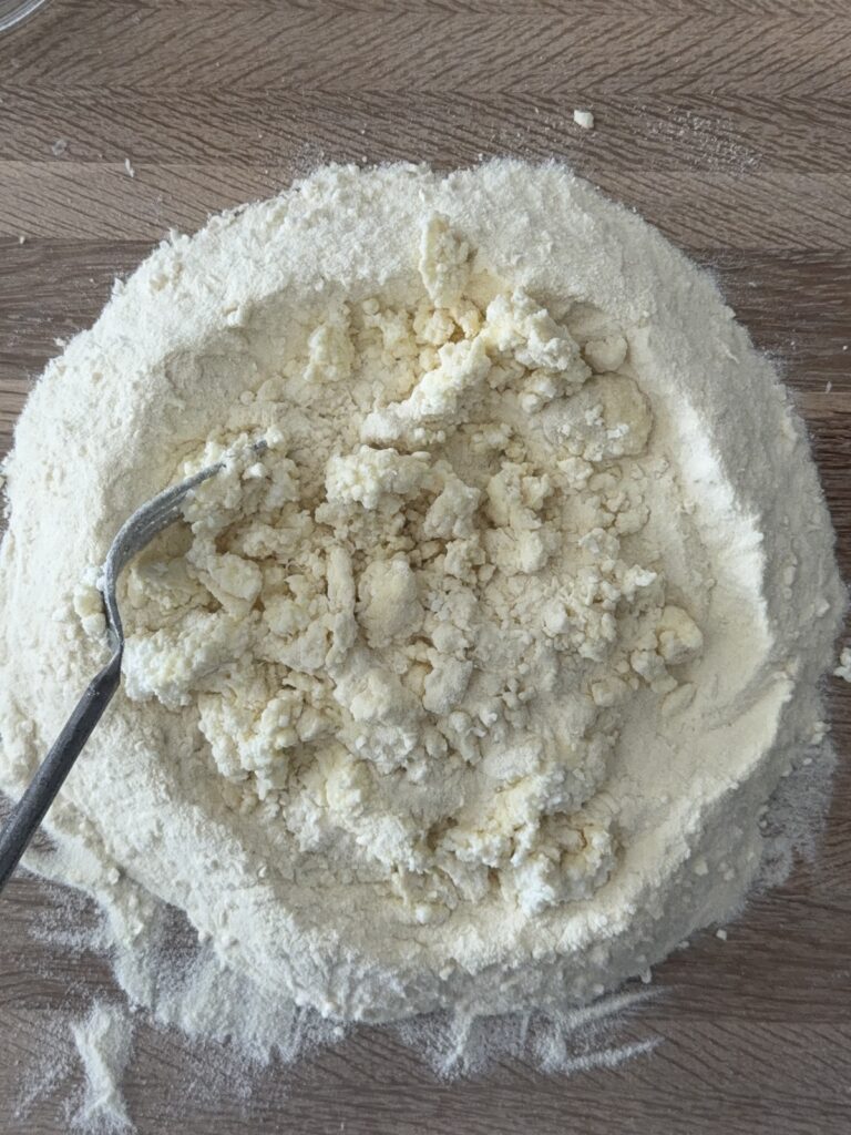 Semolina flour and ricotta mixture forming a dough well on a wooden surface with a spoon.