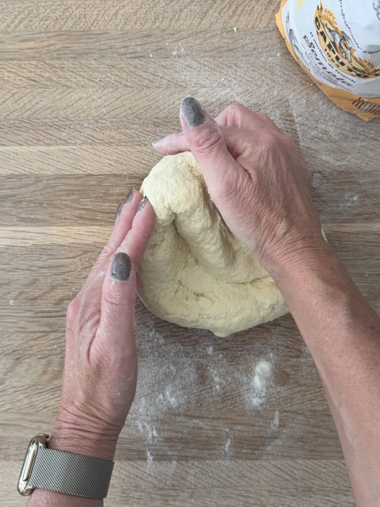 Hands kneading semolina pasta dough on a floured wooden surface.