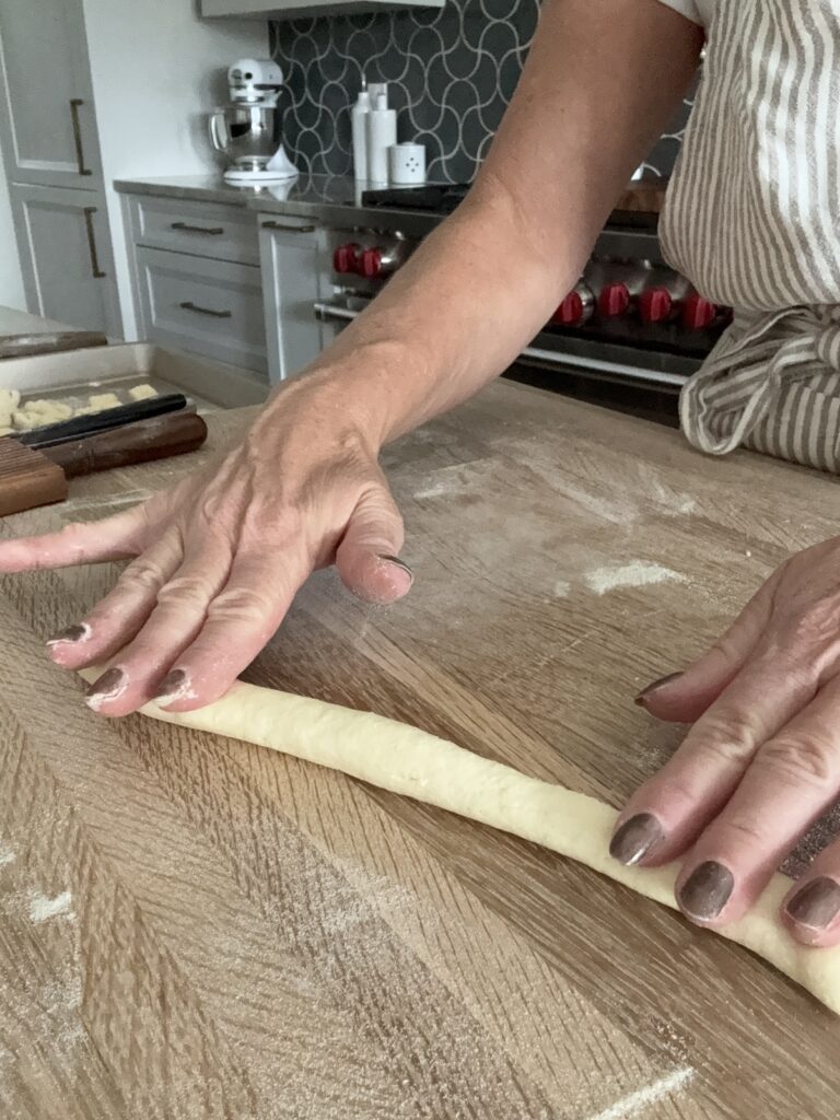 Hand rolling semolina pasta dough into a long rope on a floured wooden surface.