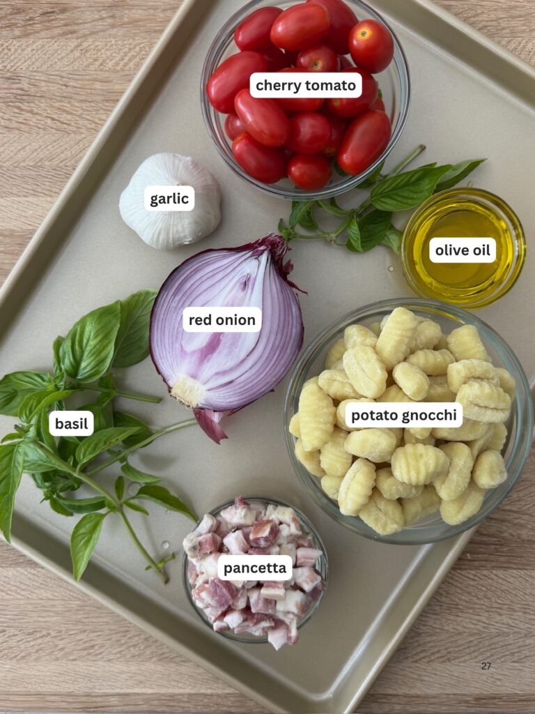 Ingredients for sheet pan gnocchi including potato gnocchi, cherry tomatoes, red onion, pancetta, garlic, basil, and olive oil arranged on a baking tray — simple Italian ingredients for an easy weeknight dinner.