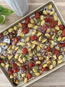 Sheet pan gnocchi with golden potato gnocchi, roasted cherry tomatoes, red onion, pancetta, garlic, and fresh basil, topped with grated Parmesan cheese on a baking sheet straight from the oven.