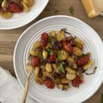 Sheet pan gnocchi with roasted cherry tomatoes, crispy potato gnocchi, red onion, pancetta, garlic, fresh basil, and Parmesan cheese served in a white bowl