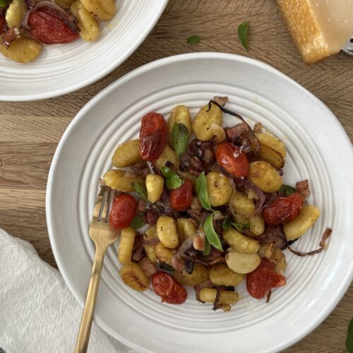Sheet pan gnocchi with roasted cherry tomatoes, crispy potato gnocchi, red onion, pancetta, garlic, fresh basil, and Parmesan cheese served in a white bowl