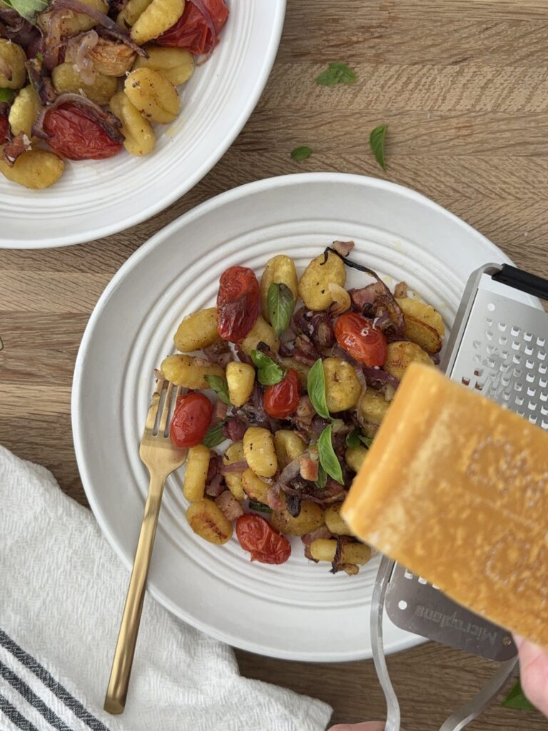 Sheet pan gnocchi with roasted cherry tomatoes, pancetta, and basil served in a white bowl, topped with freshly grated Parmesan cheese for an easy Italian-inspired dinner.
