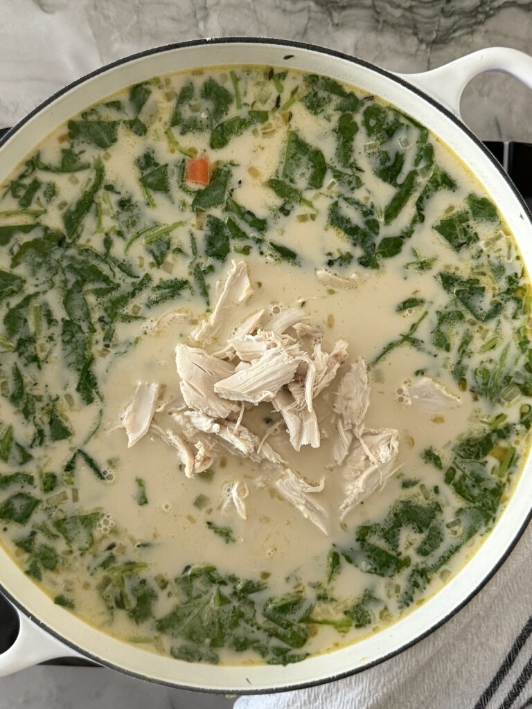 Italian chicken gnocchi soup in a white Dutch oven with creamy broth, shredded chicken, baby kale, and gnocchi.